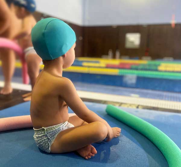 Alumno de la escuela infantil sentado de espaldas y mirando a la piscina